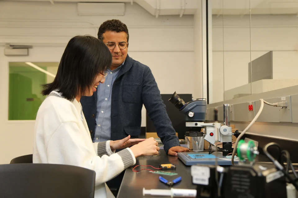 Two people working together at a laboratory bench beside a microscope